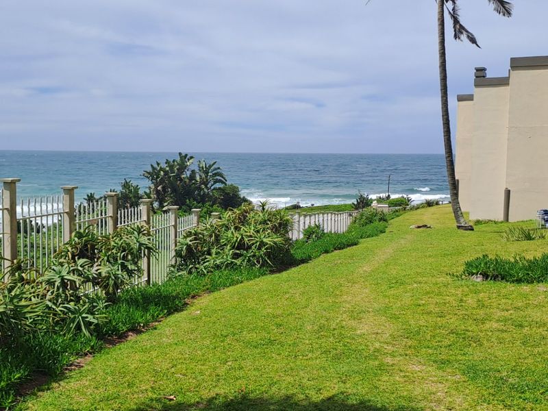 A well-maintained rear garden area featuring a lawn, perimeter fencing, and direct views of the ocean.