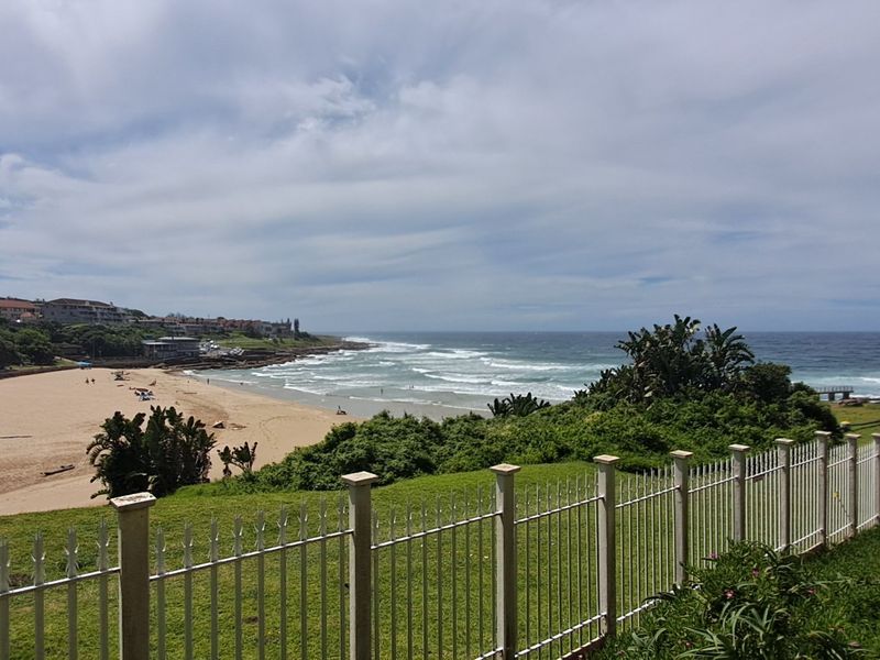 Panoramic coastal view overlooking the beach and ocean, featuring a secure metal perimeter fence in the foreground.