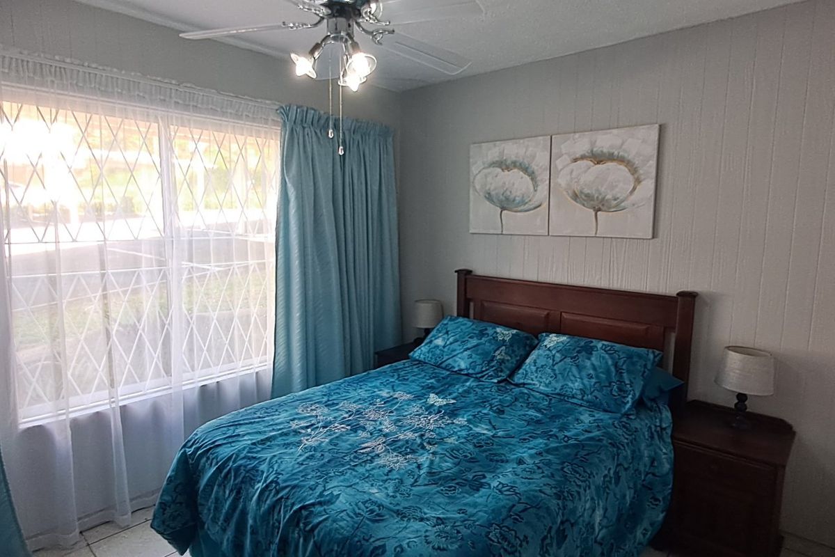 A functional bedroom featuring a ceiling fan, built-in wardrobe, and security bars on the window, providing a comfortable and secure living space.