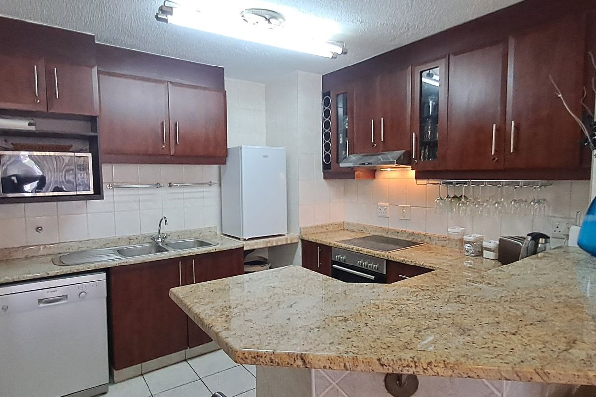 A functional kitchen featuring granite countertops, wooden cabinetry, a breakfast bar, and integrated appliances including an oven and hob.