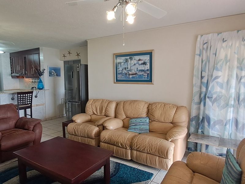 Open-plan living and kitchen area featuring tiled flooring, built-in cabinetry with granite countertops, and access to a balcony through a security gate.