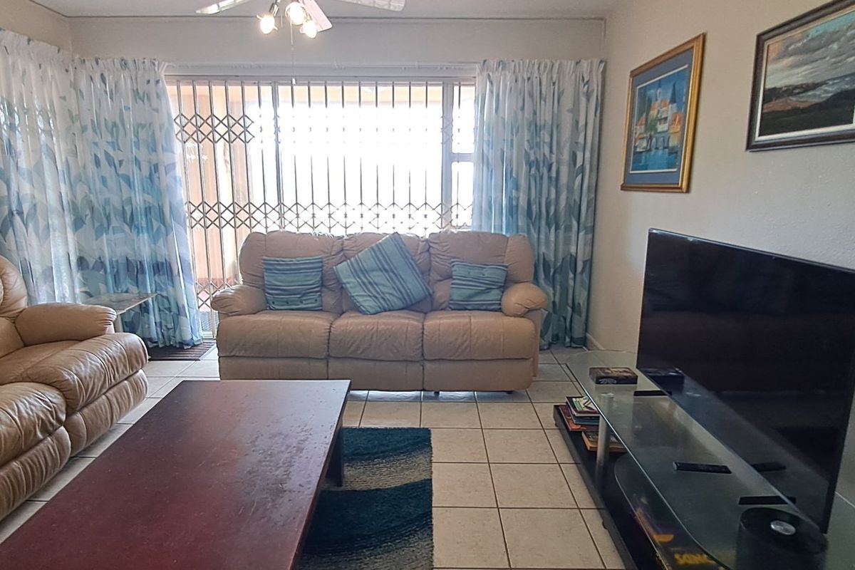 A comfortable living room featuring tiled flooring, a ceiling fan, and a sliding door with a security gate leading to the exterior.