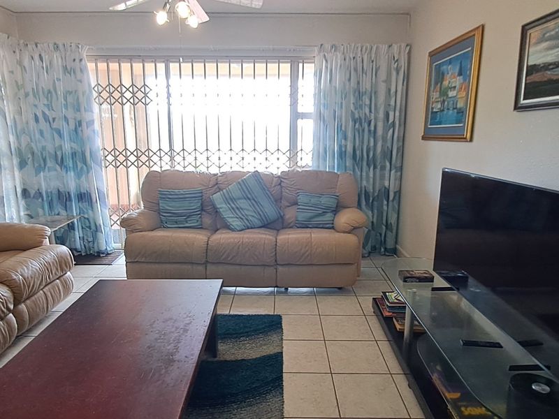 A comfortable living room featuring tiled flooring, a ceiling fan, and a sliding door with a security gate leading to the exterior.