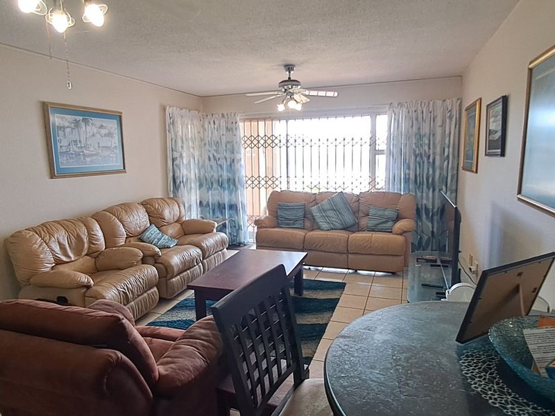 Open plan living area featuring tiled flooring, a ceiling fan, and a sliding door with security gate access to the exterior.