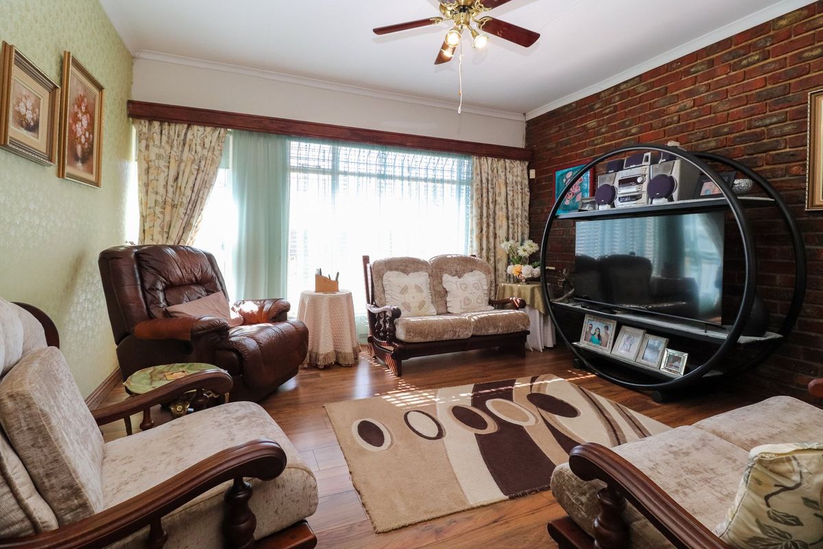 A living room featuring an exposed brick feature wall, laminate flooring, and a ceiling fan, with large windows providing natural light.