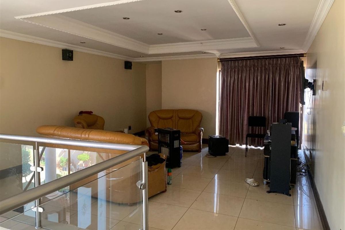 Spacious living area featuring tiled flooring, a recessed ceiling with downlights, and a modern glass and metal balustrade overlooking the lower level.
