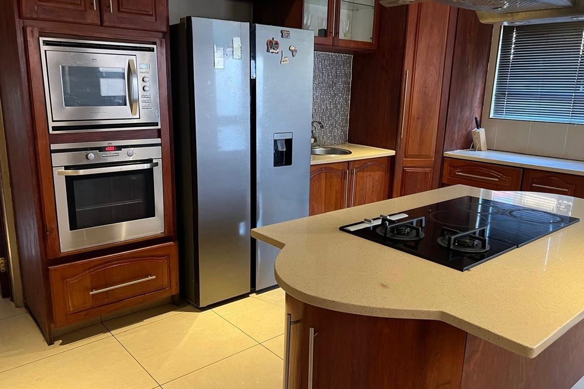 A well-equipped kitchen featuring dark wood cabinetry, stone countertops, a central island with a hob, and integrated stainless steel appliances.