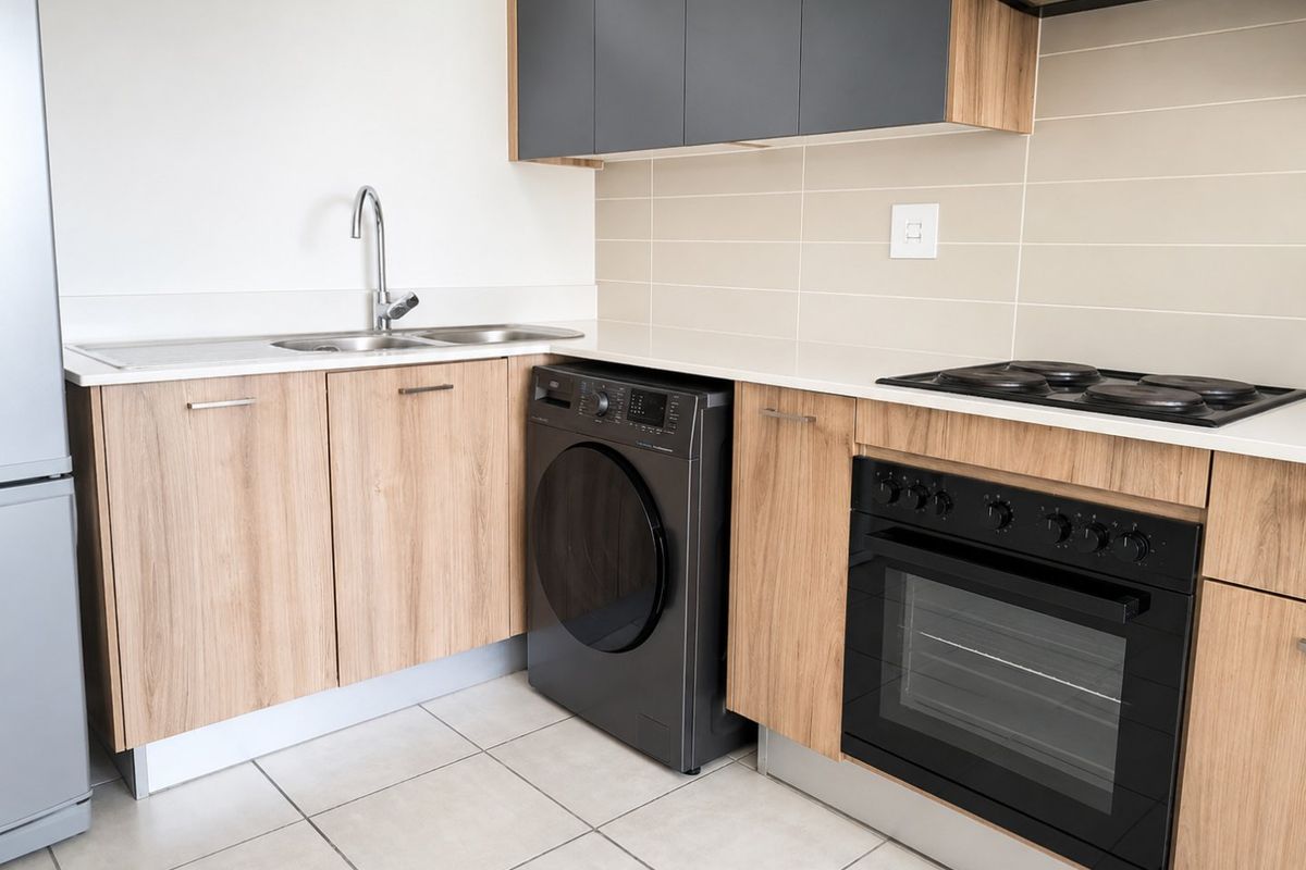 Modern kitchen featuring wood-finish cabinetry, dark grey upper cupboards, integrated oven and hob, and a stainless steel sink with tiled backsplash.