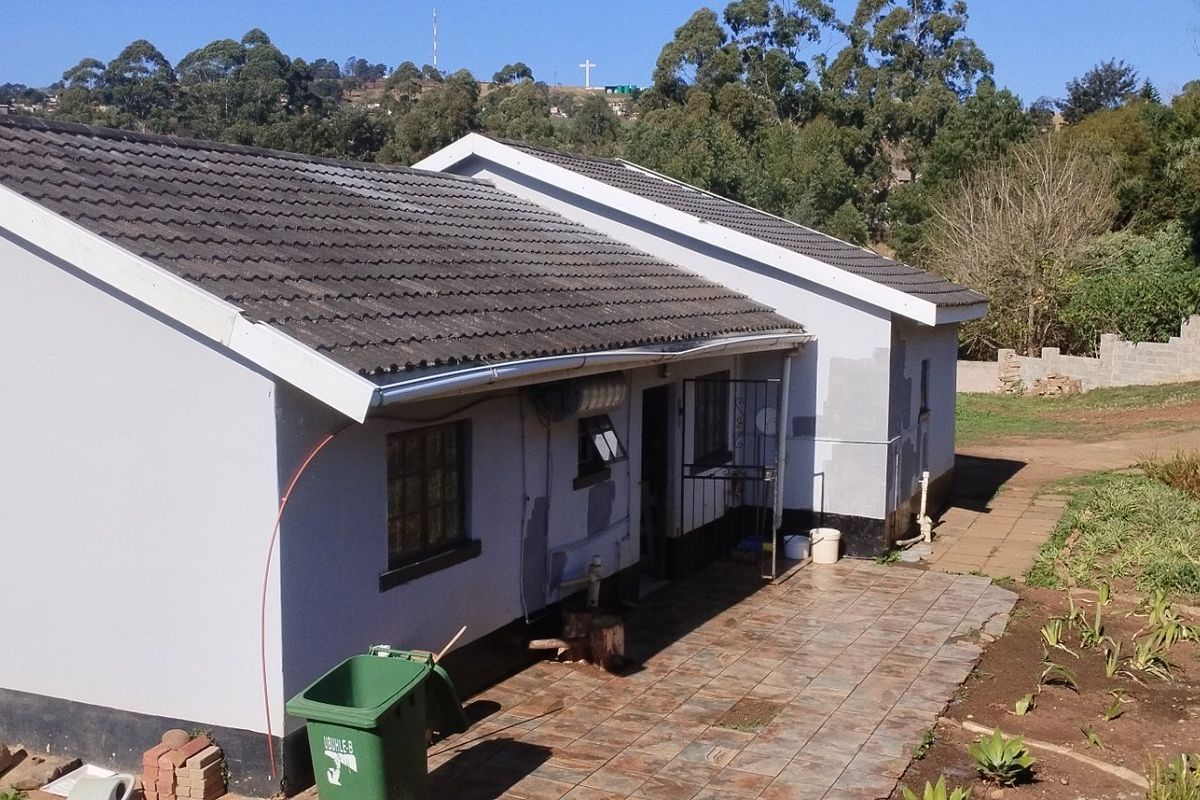 Rear view of the house featuring a tiled roof, paved patio area, and unfinished exterior wall surfaces.