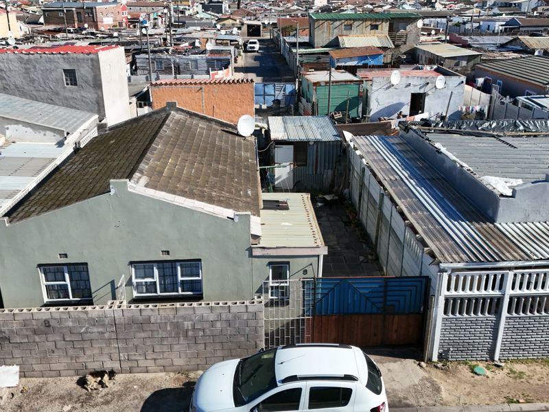 Aerial view of a residential property featuring a tiled roof, concrete boundary walls, and metal gate access within a dense urban neighborhood.