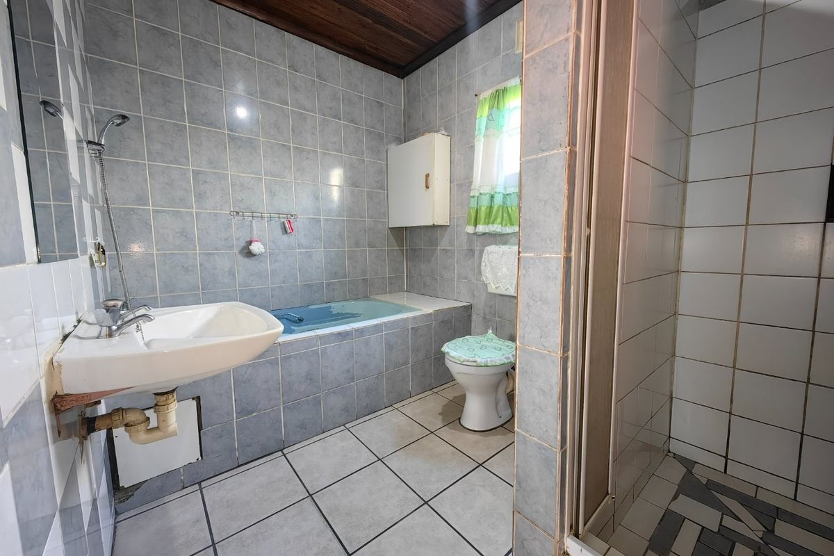 A dated bathroom featuring a built-in bathtub, separate shower enclosure, wall-mounted basin, and tiled finishes with a timber ceiling.