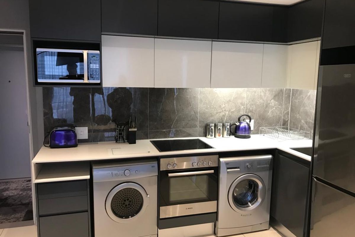 Modern kitchen featuring sleek two-tone cabinetry, stone splashback, integrated oven and hob, and built-in microwave with under-cabinet lighting.