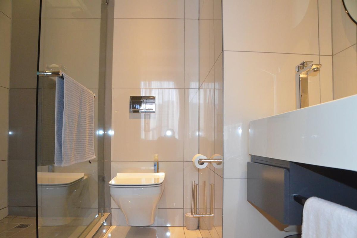 Modern bathroom featuring a wall-mounted toilet, glass shower enclosure, and a sleek vanity basin with contemporary chrome fixtures and neutral wall tiling.
