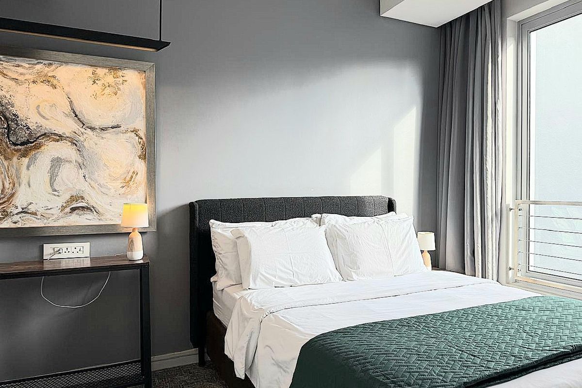 A well-maintained bedroom featuring neutral grey walls, large window with curtains, and modern recessed lighting.