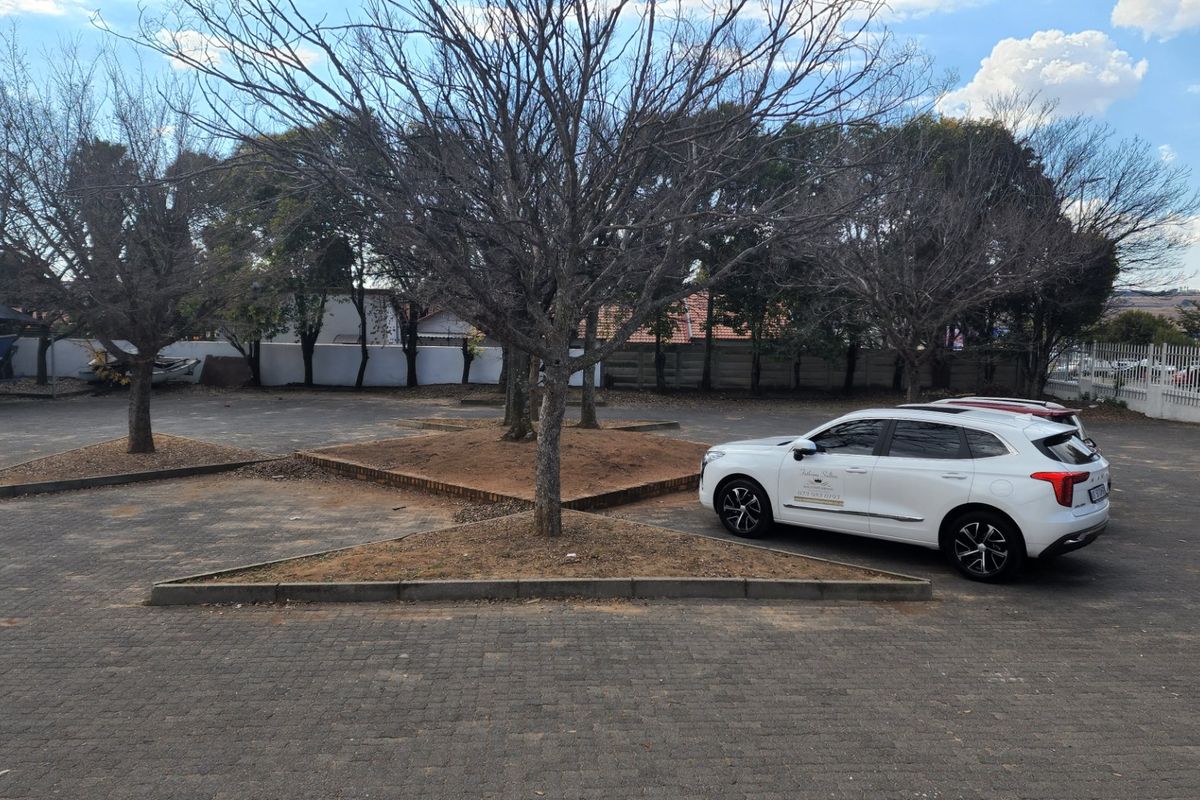 A paved driveway area featuring brick-edged garden beds and perimeter fencing, providing ample space for vehicle parking.
