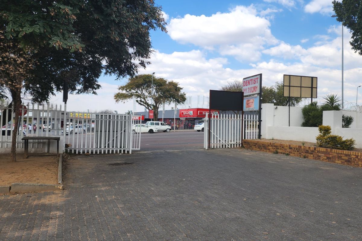 A view of the property entrance featuring a paved driveway, security gate, and perimeter wall with razor wire, overlooking a commercial area.