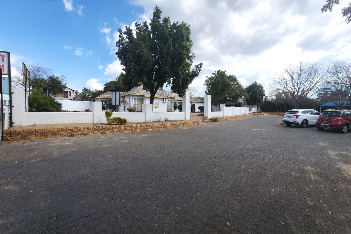 Front exterior view of the property featuring a large paved driveway, perimeter walling, and a brick retaining wall.