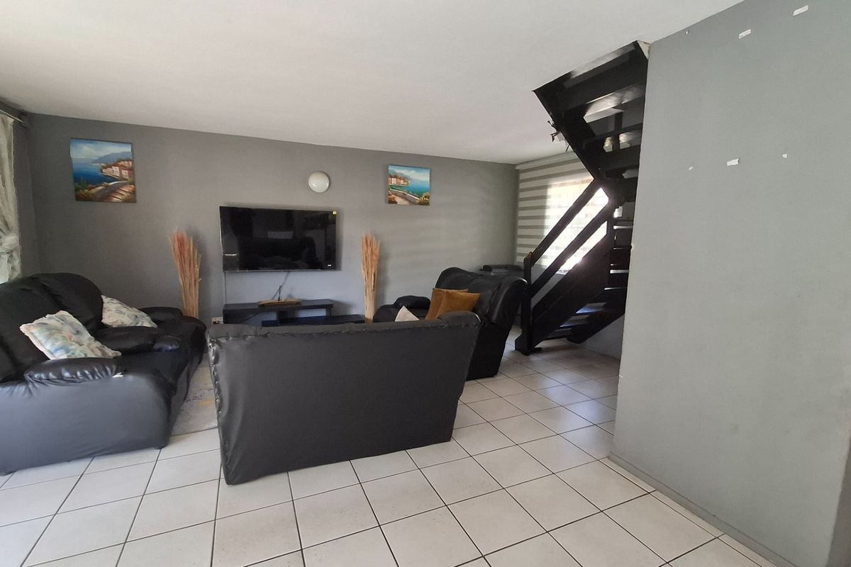 Spacious living room featuring ceramic floor tiles and a prominent staircase, offering a functional layout with neutral wall tones.