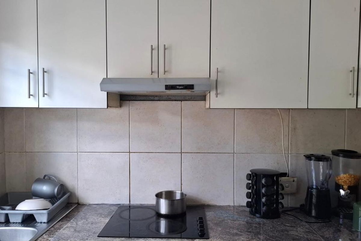 A functional kitchen area featuring white cabinetry, a ceramic hob, an extractor fan, and a tiled splashback with stone countertops.