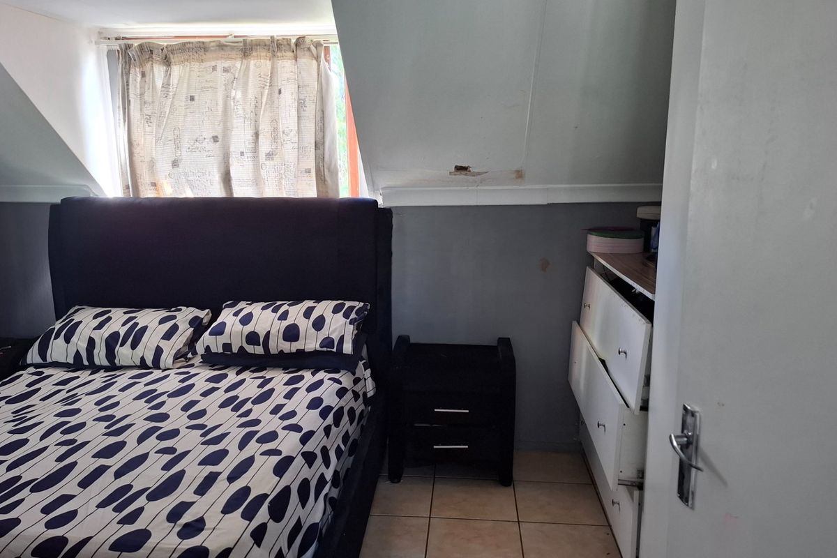A bedroom featuring tiled flooring and a sloped ceiling, showing signs of wear including damaged plaster and peeling paint.
