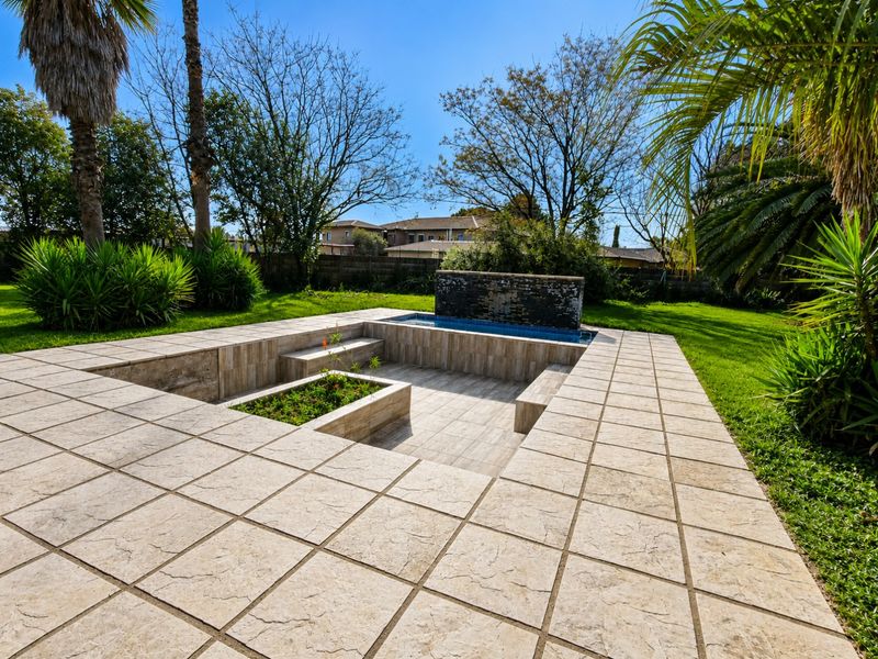 A well-maintained outdoor entertainment area featuring a sunken tiled patio, built-in seating, a central planter box, and a modern water feature.