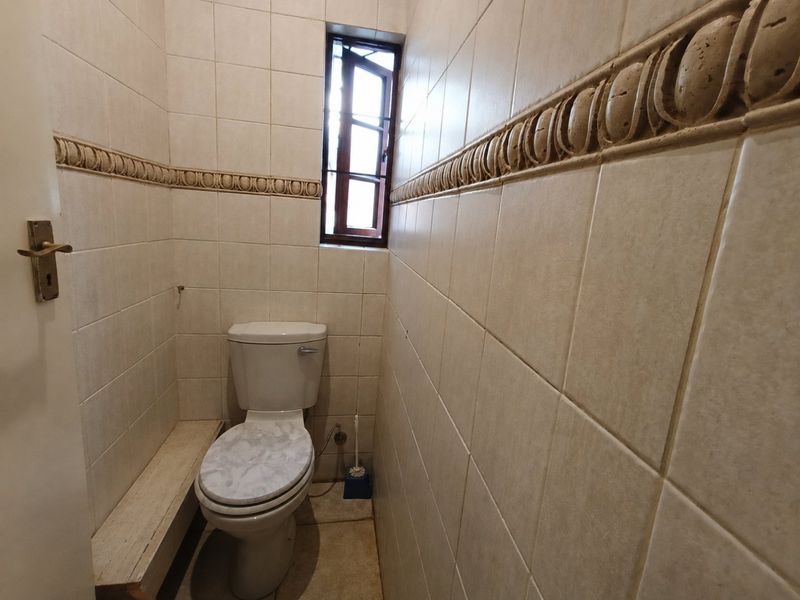 A compact guest bathroom featuring full-height ceramic wall tiling with a decorative border and a small casement window.