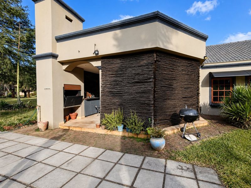 Covered outdoor patio area featuring a built-in braai, sink, and tiled flooring, providing a functional space for outdoor entertaining and dining.