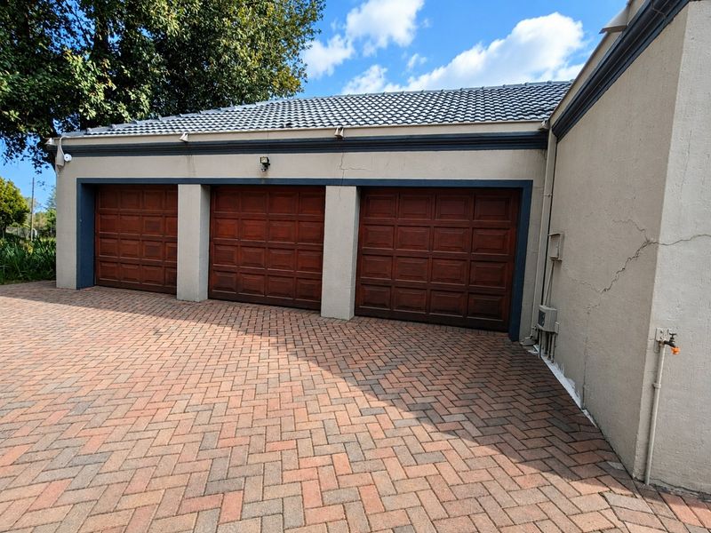 A triple garage with wooden doors and a paved driveway, featuring visible exterior wall cracks requiring maintenance.