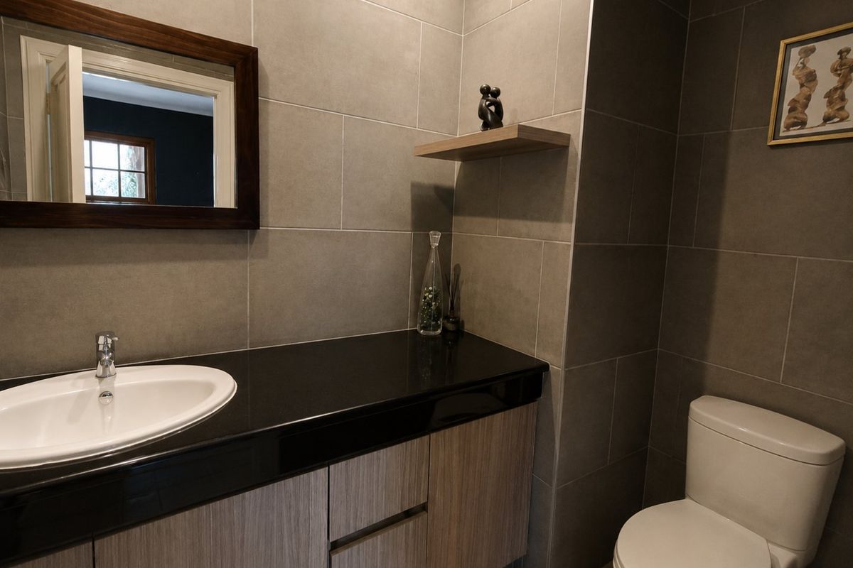 Modern bathroom featuring a sleek vanity with granite countertop, drop-in basin, and contemporary grey wall tiling.