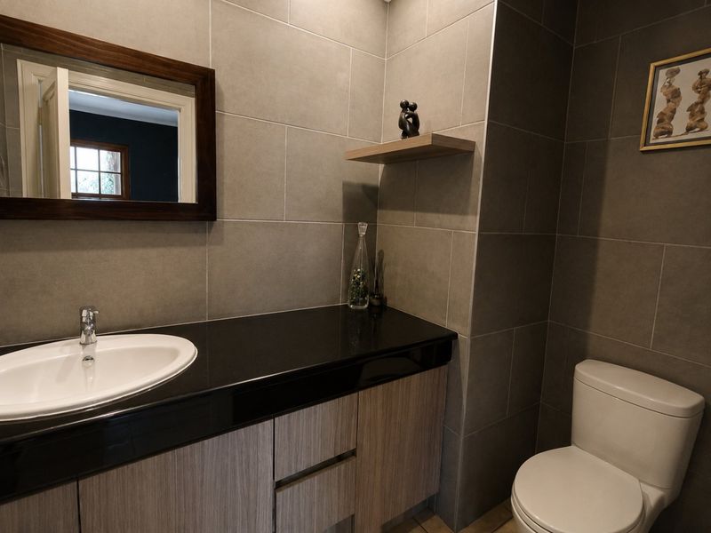 Modern bathroom featuring a sleek vanity with granite countertop, drop-in basin, and contemporary grey wall tiling.