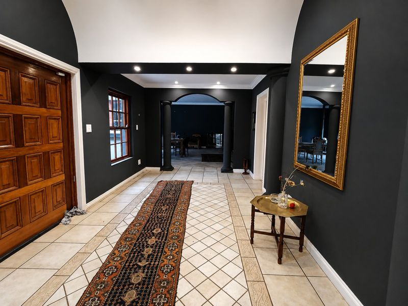 A spacious entrance hall featuring a vaulted ceiling, tiled flooring, and elegant dark-toned walls, leading through an archway into the main living area.