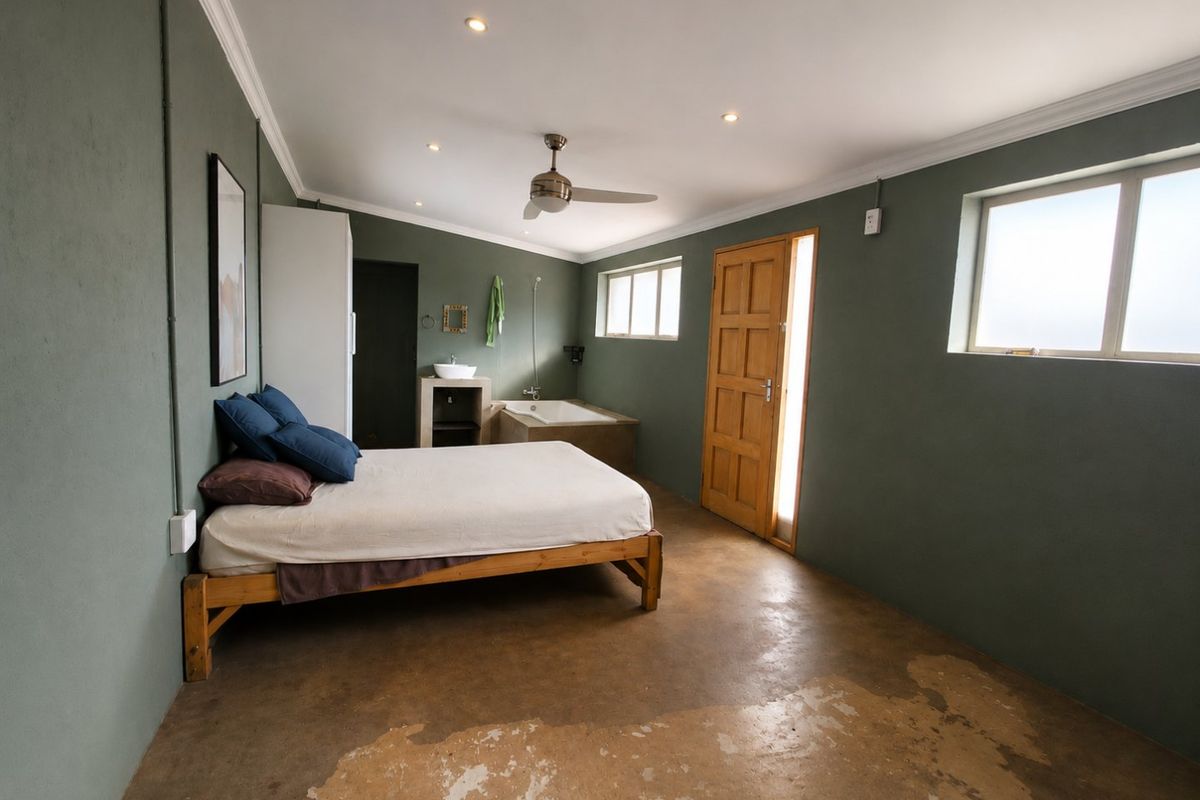Spacious bedroom featuring an open-plan en-suite bathroom with a built-in bathtub, vessel sink, and polished concrete flooring.