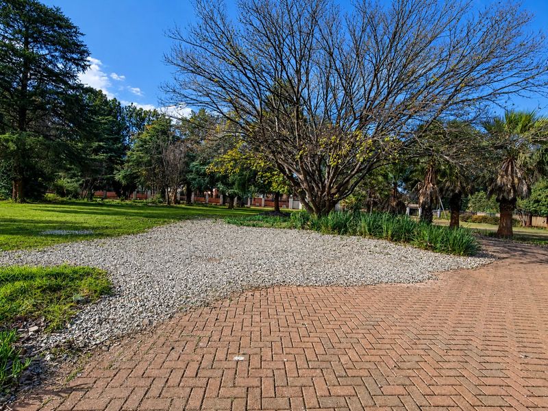A spacious garden area featuring a brick-paved driveway, gravel landscaping, and mature trees, offering a well-maintained outdoor space.