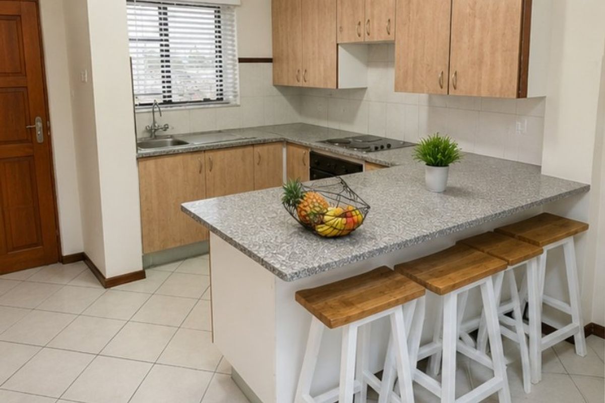 Functional kitchen featuring light wood-tone cabinetry, granite-look countertops, a breakfast bar, and built-in appliances, finished with neutral floor tiles.