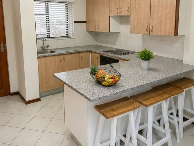 Functional kitchen featuring light wood-tone cabinetry, granite-look countertops, a breakfast bar, and built-in appliances, finished with neutral floor tiles.