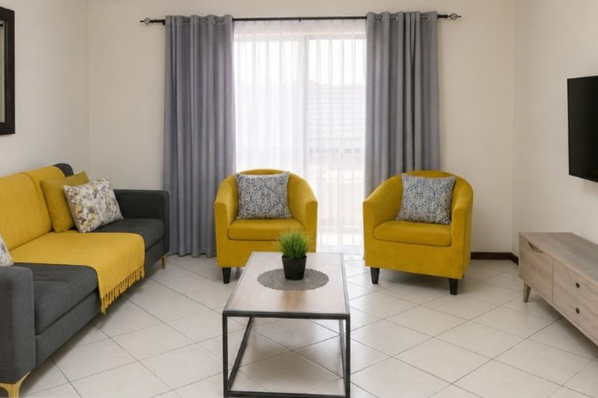 A bright and well-maintained living room featuring neutral tiled flooring and a sliding glass door with curtains, providing access to the exterior.