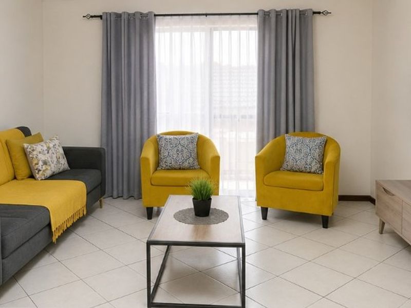 A bright and well-maintained living room featuring neutral tiled flooring and a sliding glass door with curtains, providing access to the exterior.
