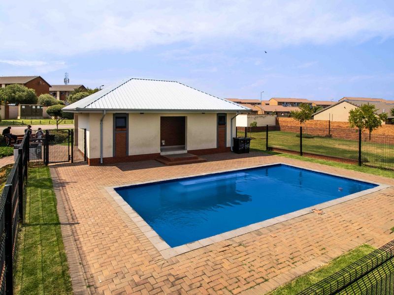 A well-maintained communal swimming pool area featuring a paved deck, perimeter fencing, and a small utility structure with a metal roof.
