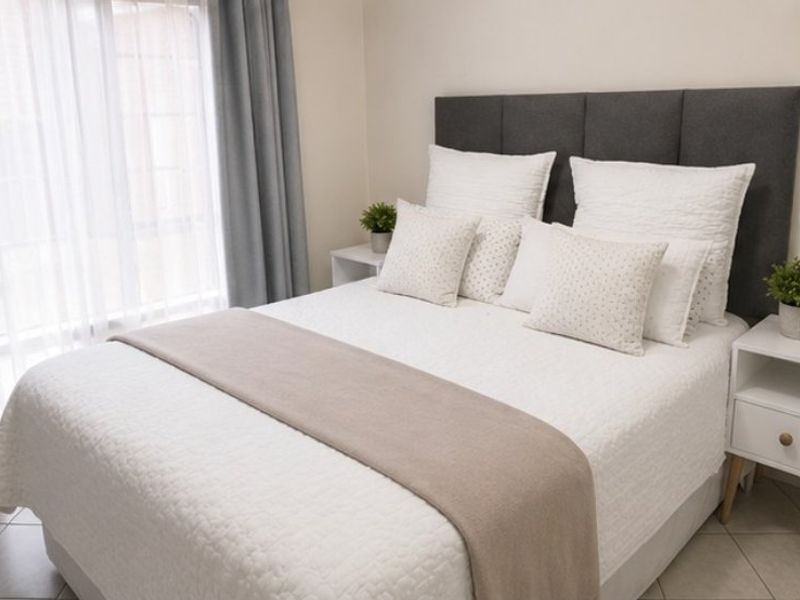 A well-maintained bedroom featuring neutral wall tones, tiled flooring, and large windows with installed curtain tracks.