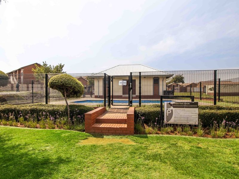 A communal swimming pool area featuring a secure mesh fence, brick access steps, and well-maintained surrounding garden space.