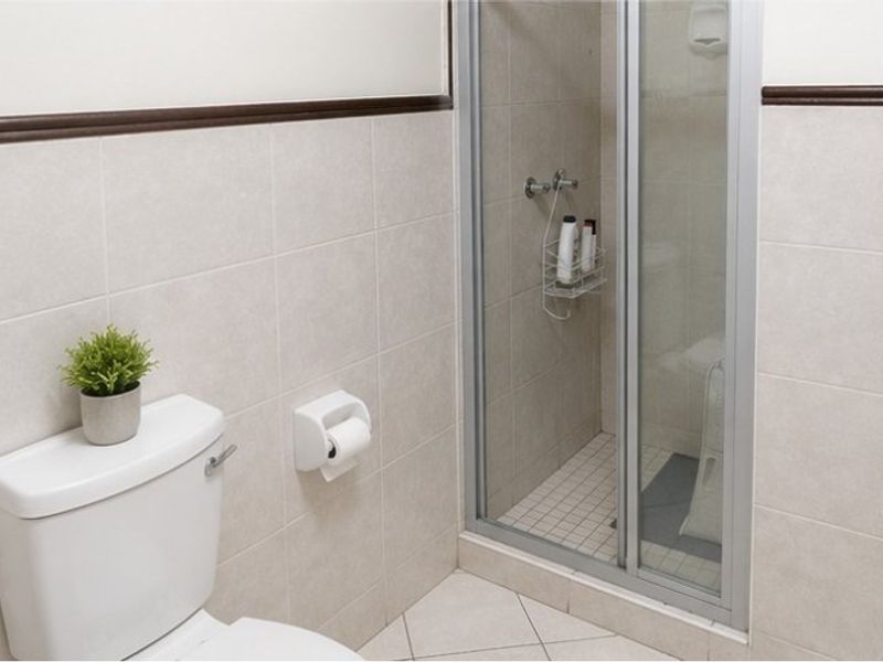 A functional bathroom featuring a standard toilet and a glass-enclosed shower with neutral ceramic wall and floor tiling.