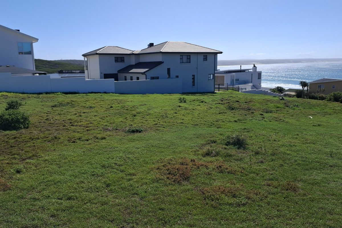 A vacant residential plot featuring a grassy landscape with a boundary wall and scenic coastal views.