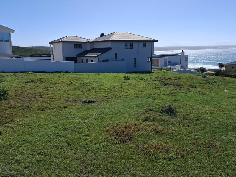A vacant residential plot featuring a grassy landscape with a boundary wall and scenic coastal views.