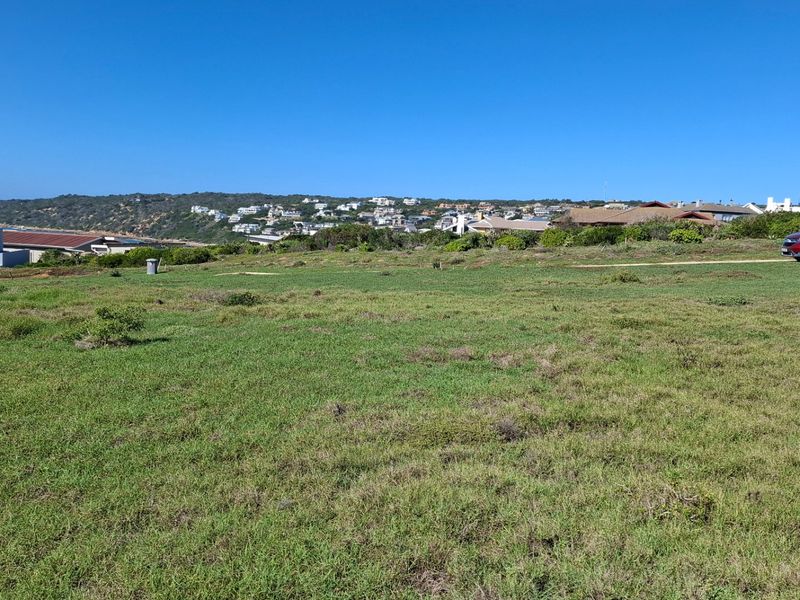 A wide-angle view of a vacant residential plot overlooking a coastal neighborhood and surrounding landscape under a clear blue sky.