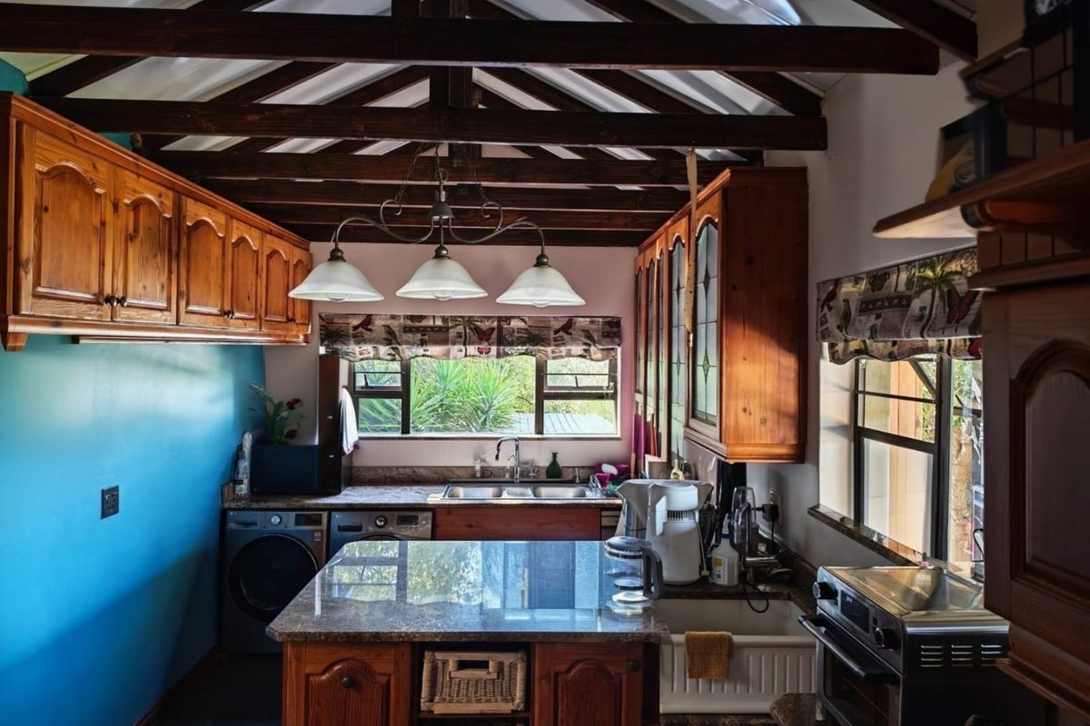 A rustic kitchen featuring exposed timber beams, granite countertops, a farmhouse sink, and warm timber cabinetry with integrated laundry facilities.