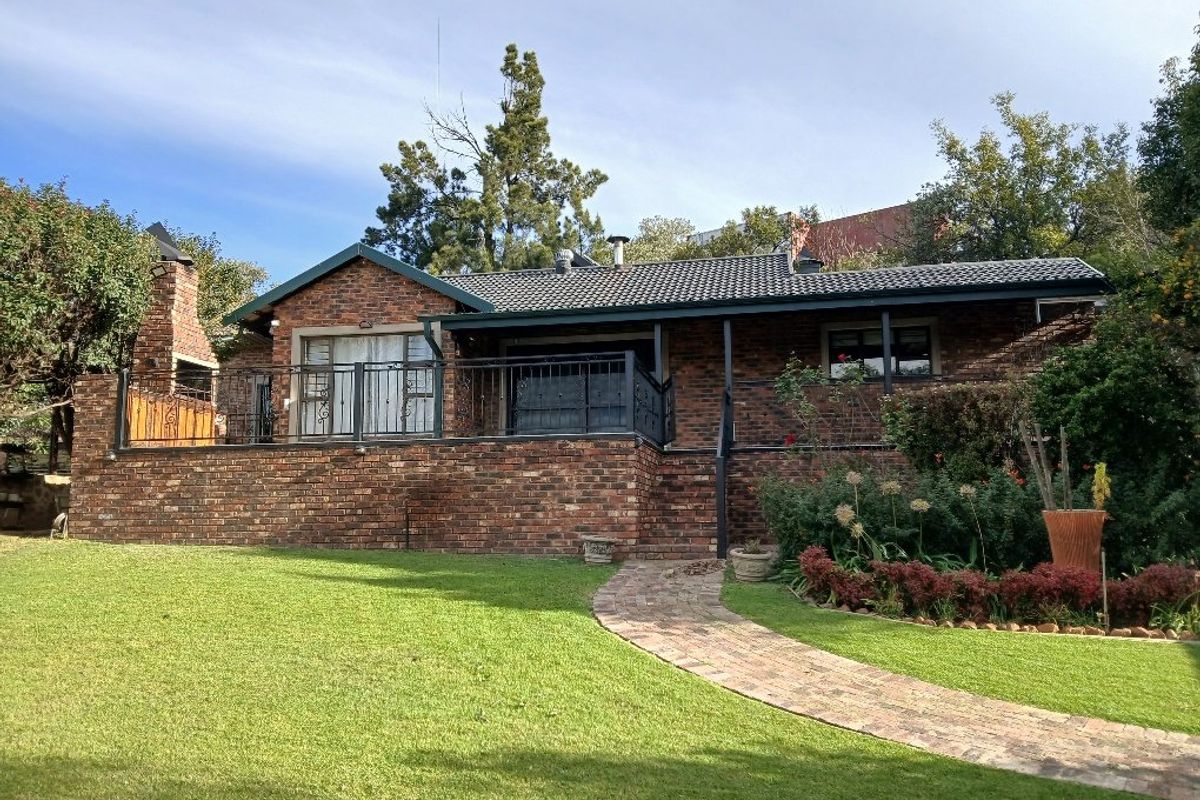 Rear view of a brick house featuring a raised patio with wrought iron railings, a built-in brick braai, and a well-maintained garden with paved path.