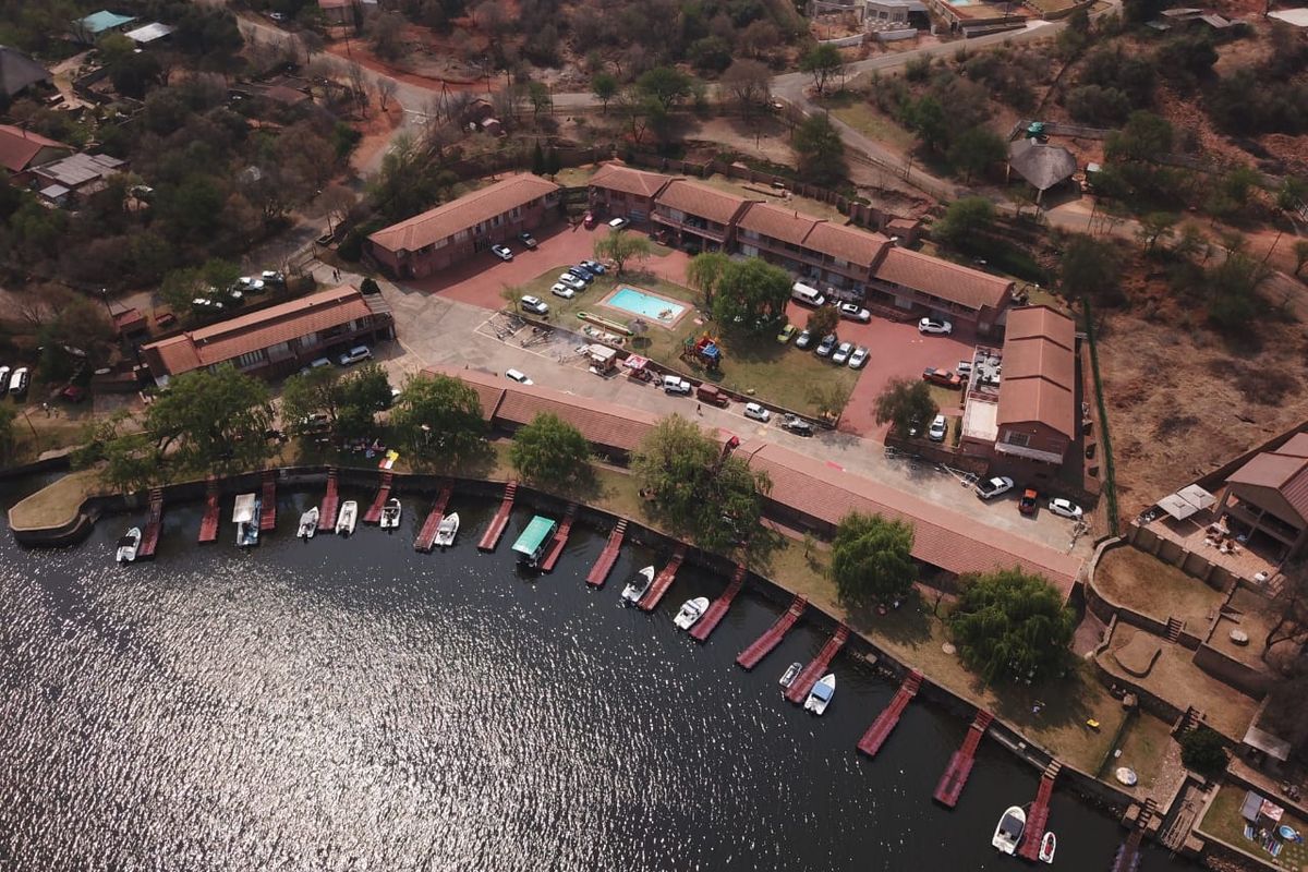 Aerial view of a waterfront residential complex featuring a central swimming pool, paved parking areas, and private boat jetties along the shoreline.