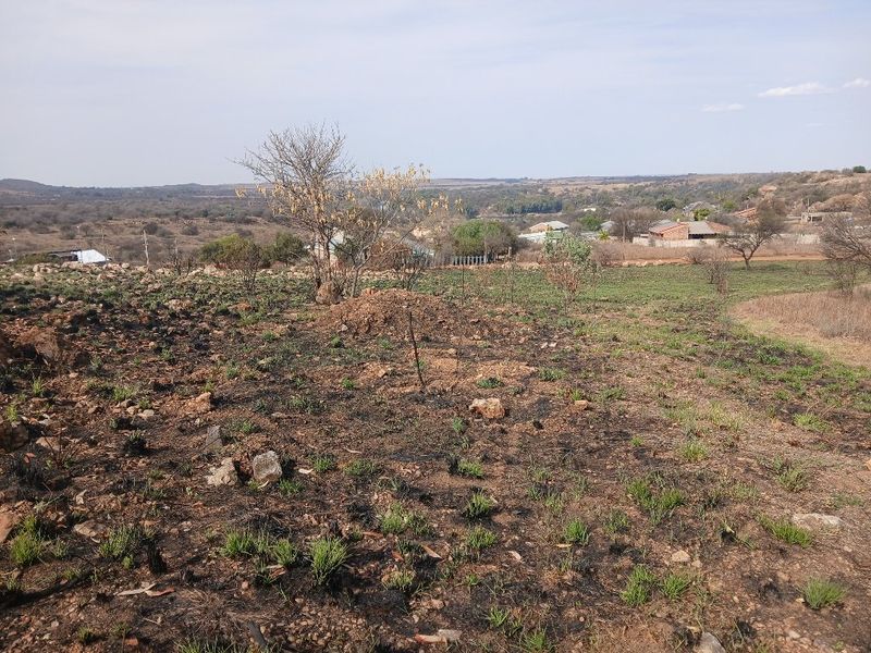 A wide-angle view of the vacant residential land, showing natural terrain and surrounding landscape with signs of recent vegetation clearing or fire damage.