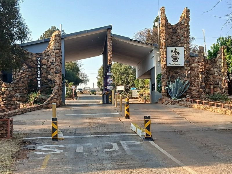 The entrance to Vaaloewer featuring a stone masonry gatehouse, security boom gate, and paved driveway access.