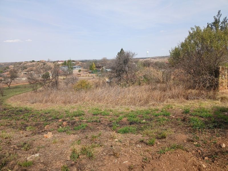 A view of the vacant residential land featuring natural vegetation and sloped terrain with surrounding neighborhood landscape in the distance.